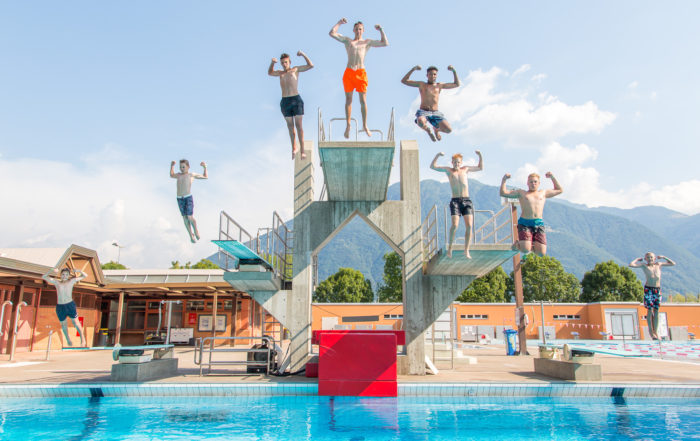 Acht Jungs springen gleichzeitig in derselben Pose von fünf verschiedenen Sprungbrettern ins Wasser