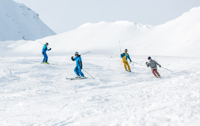 Eine Gruppe von vier Skifahrern fährt hintereinander über die Piste